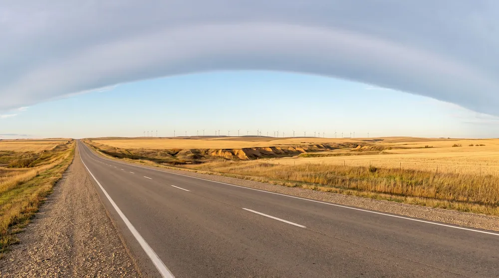 Straight prairie highway under a chinook arch